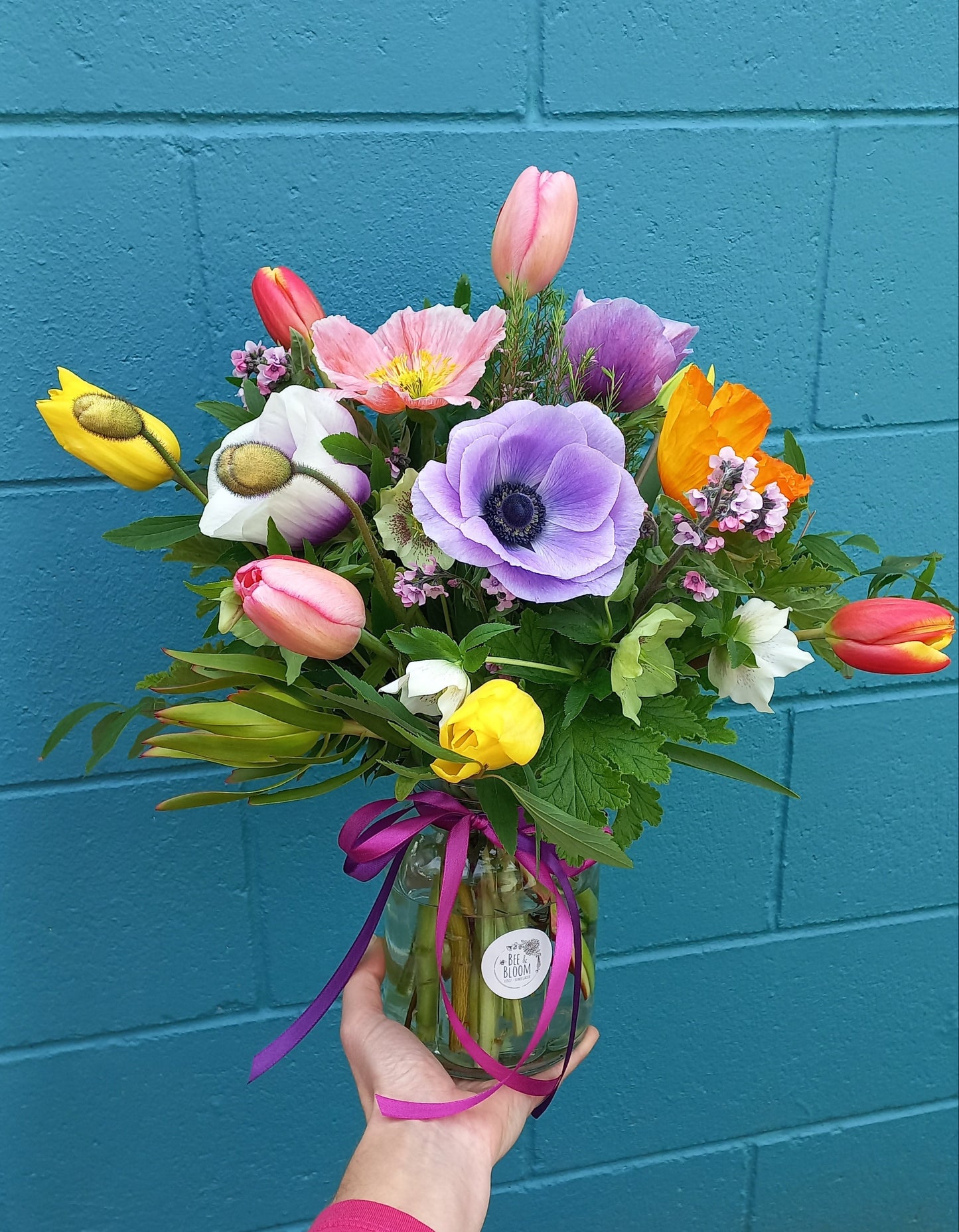 Bouquet of colorful flowers held by a person against a blue tiled wall.