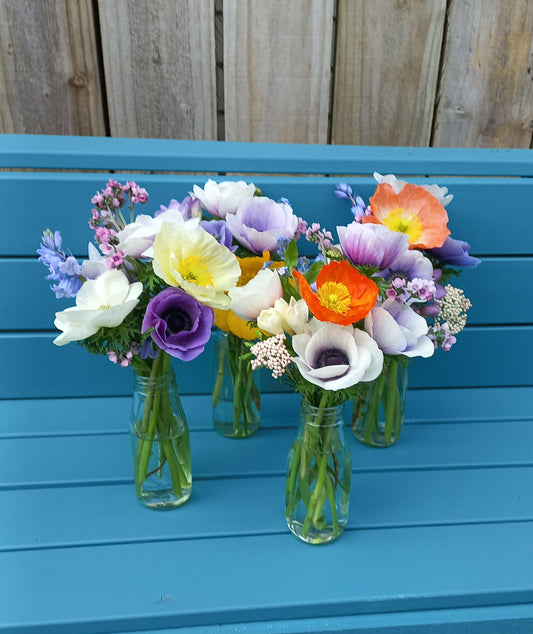 Colorful flowers arranged on green bottles against a blue wooden background