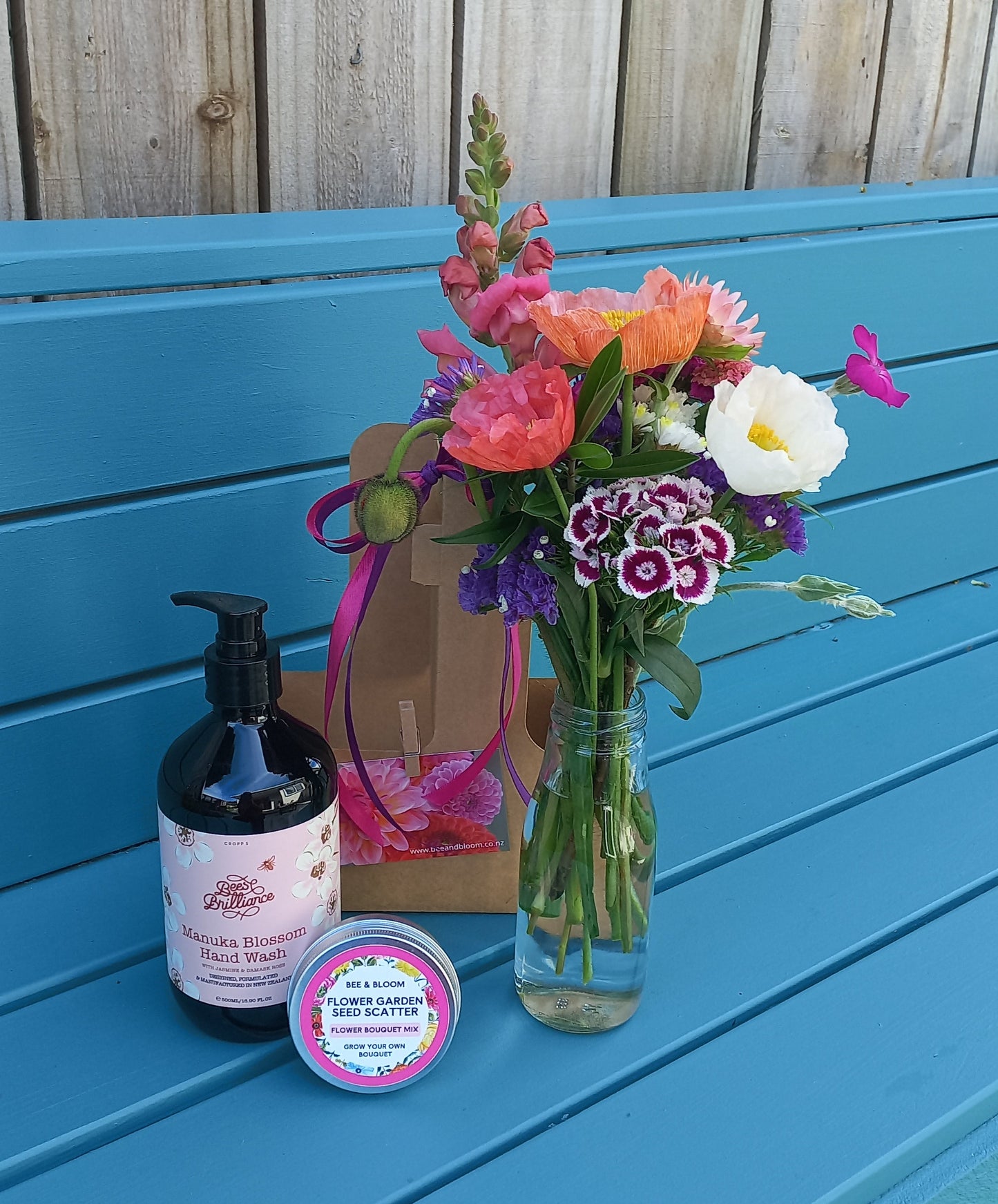 Bouquet of flowers and a bottle on a blue surface next to wooden planks.