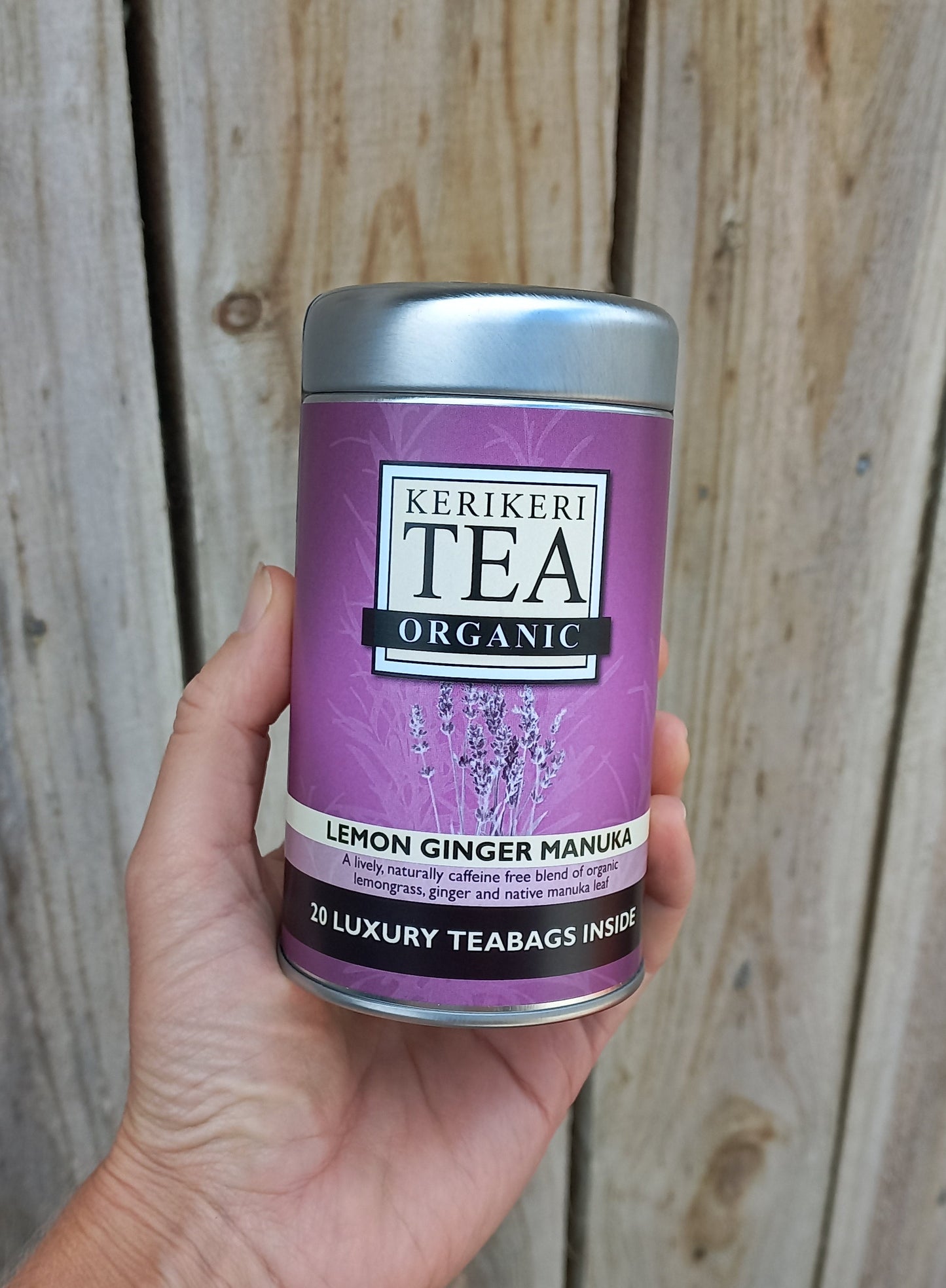 Hand holding a purple and silver tea canister on a wooden surface
