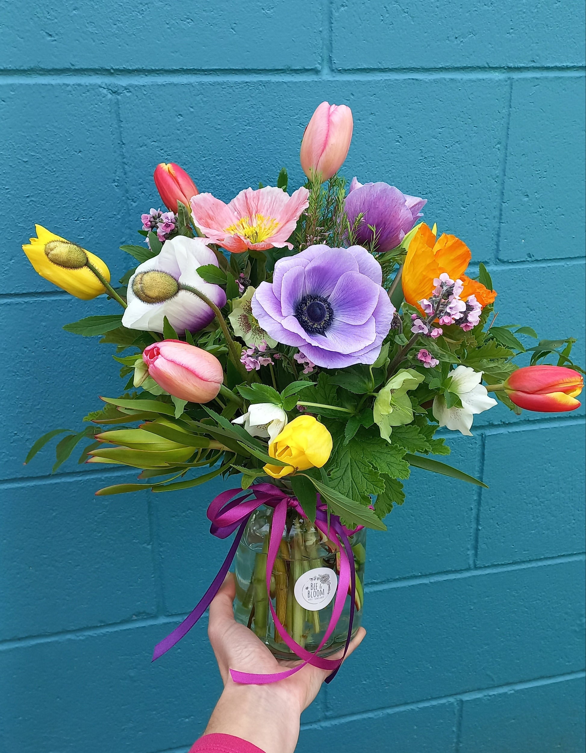 Bouquet of colorful flowers held by a person against a blue tiled wall.