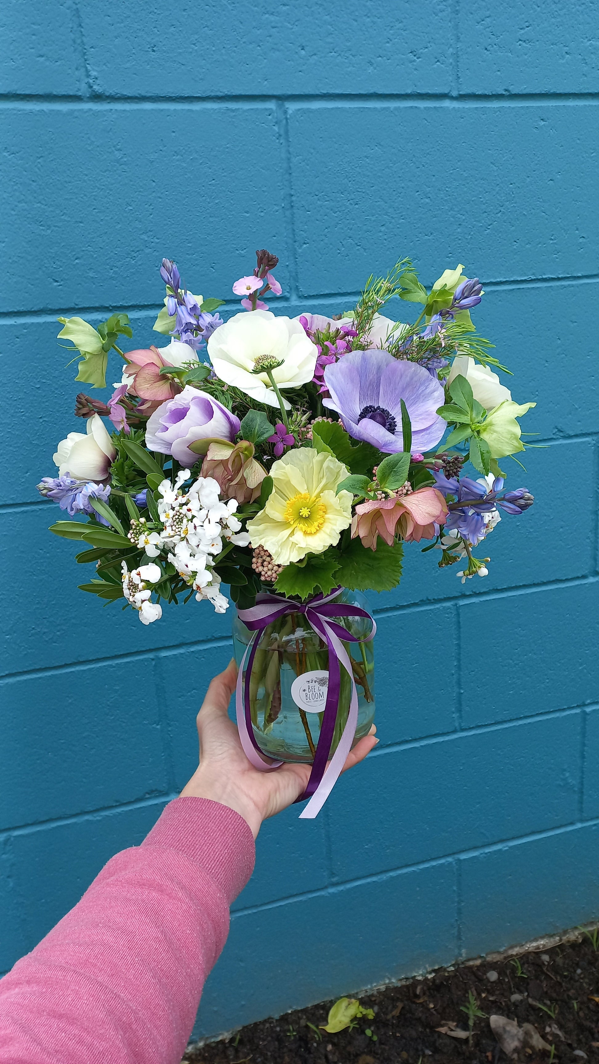 condolence flower arrangement in a glass vase against a blue wall
