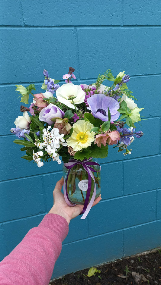 condolence flower arrangement in a glass vase against a blue wall
