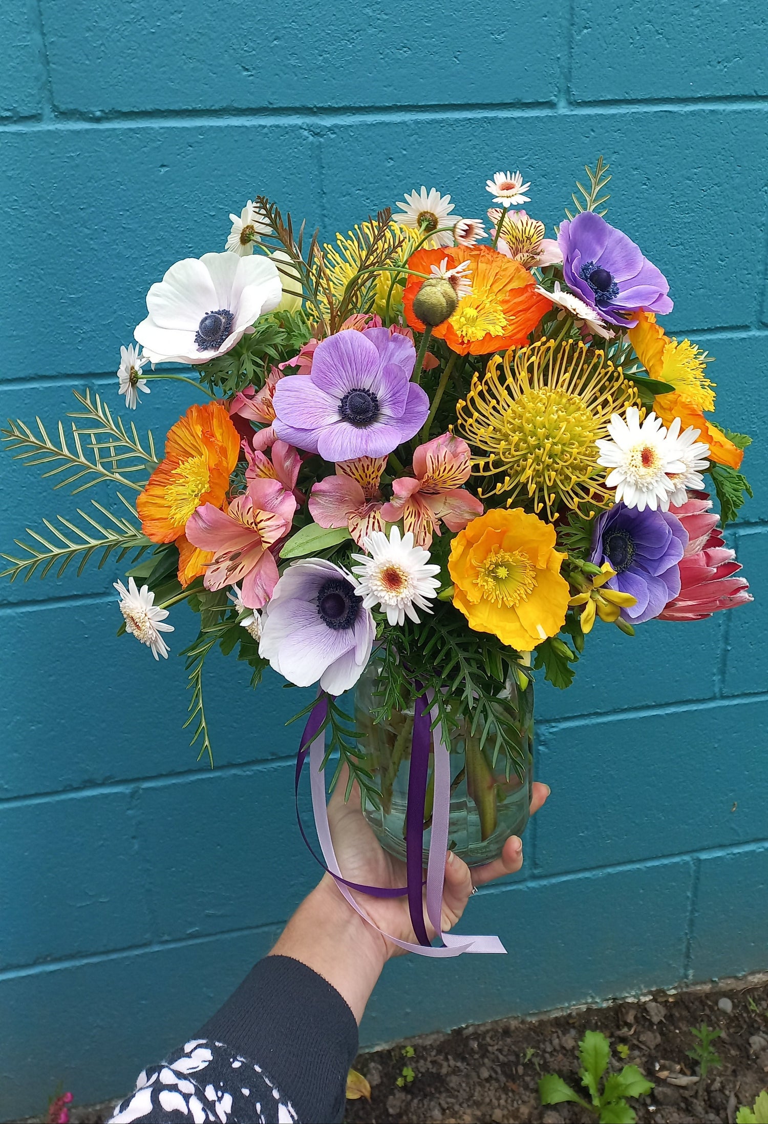 Bouquet of colorful flowers held against a teal wall