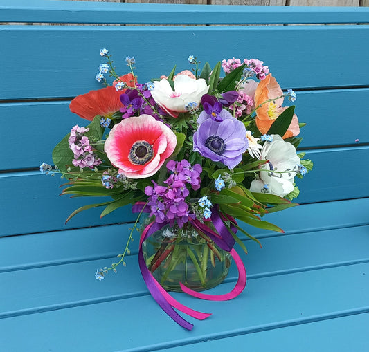 Bouquet of colorful flowers in a clear vase with ribbons on a blue wooden surface