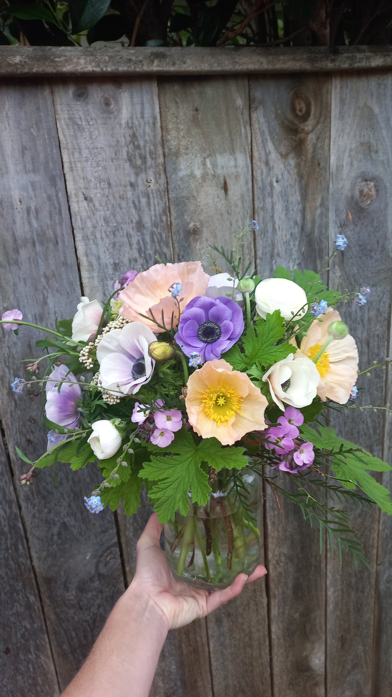 Hand holding a bouquet of flowers against a wooden background