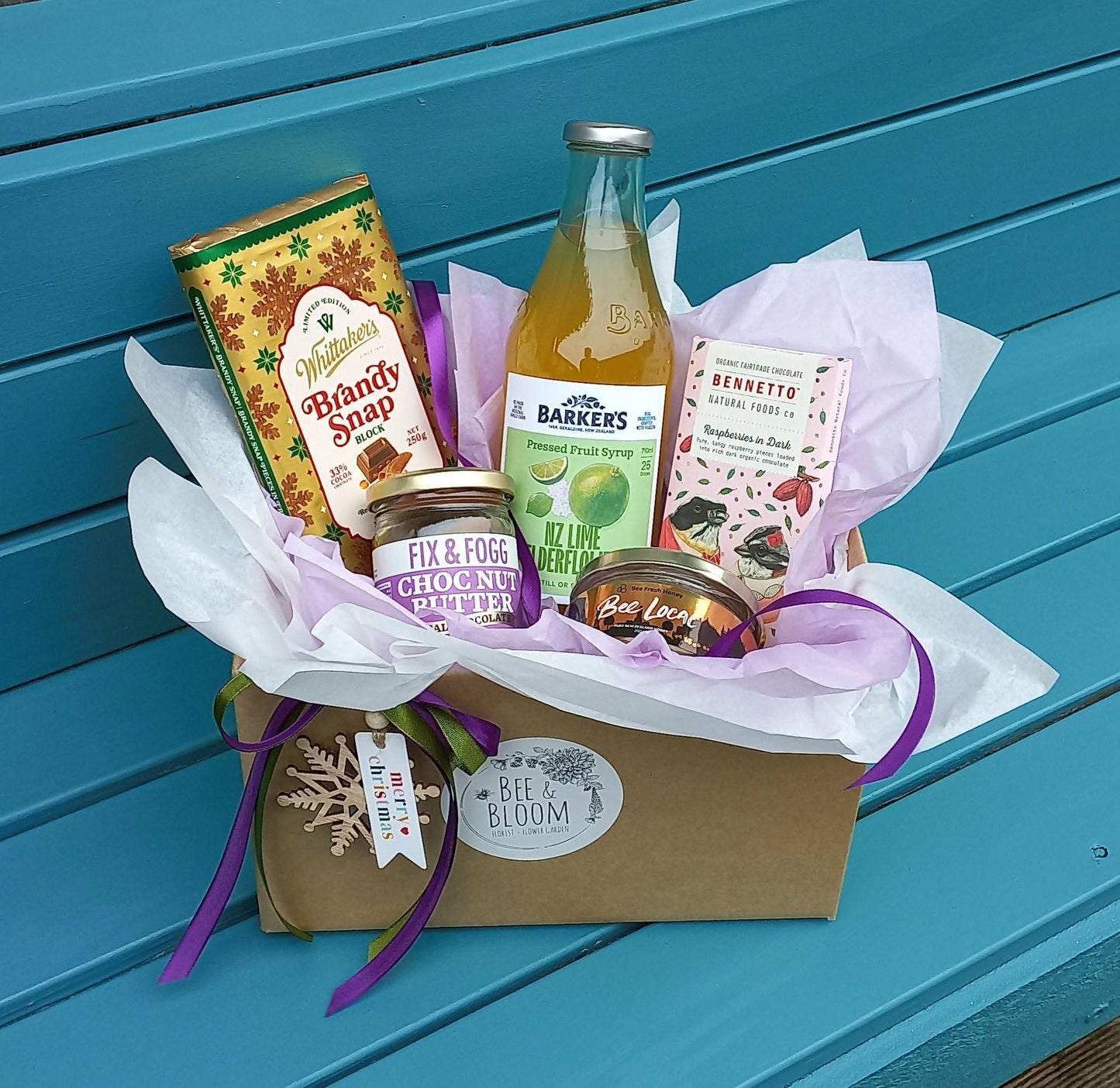 Gift basket with a bottle of juice on a blue bench outdoors.