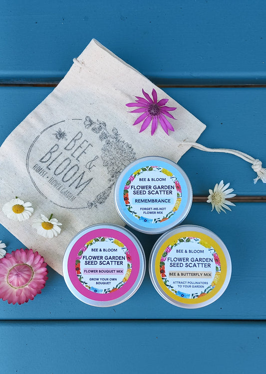 Three small containers with colorful labels on a blue wooden surface with flowers and a bag.