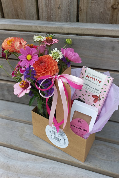 Bouquet of flowers with a pink ribbon and a box of chocolates on a wooden surface