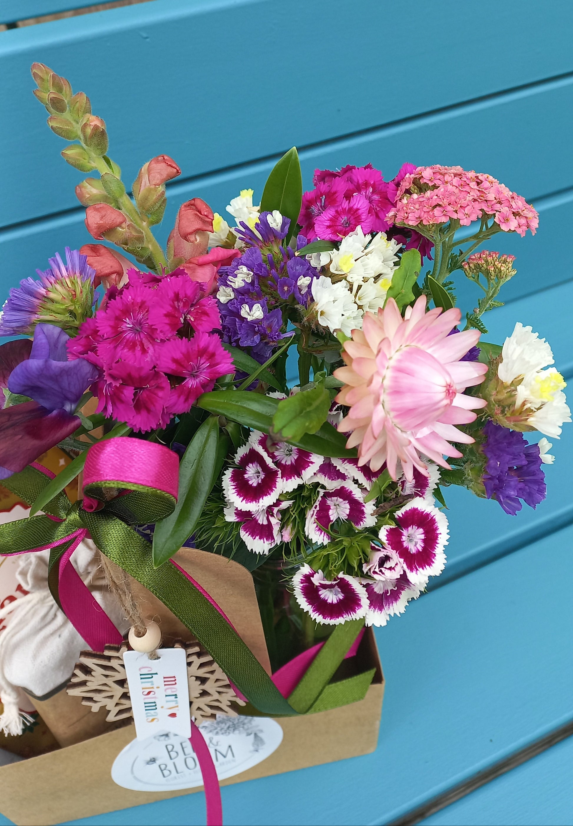 Bouquet of colorful flowers with a pink ribbon against a blue chair.