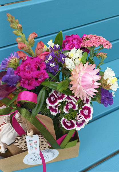 Bouquet of colorful flowers with a pink ribbon against a blue chair.