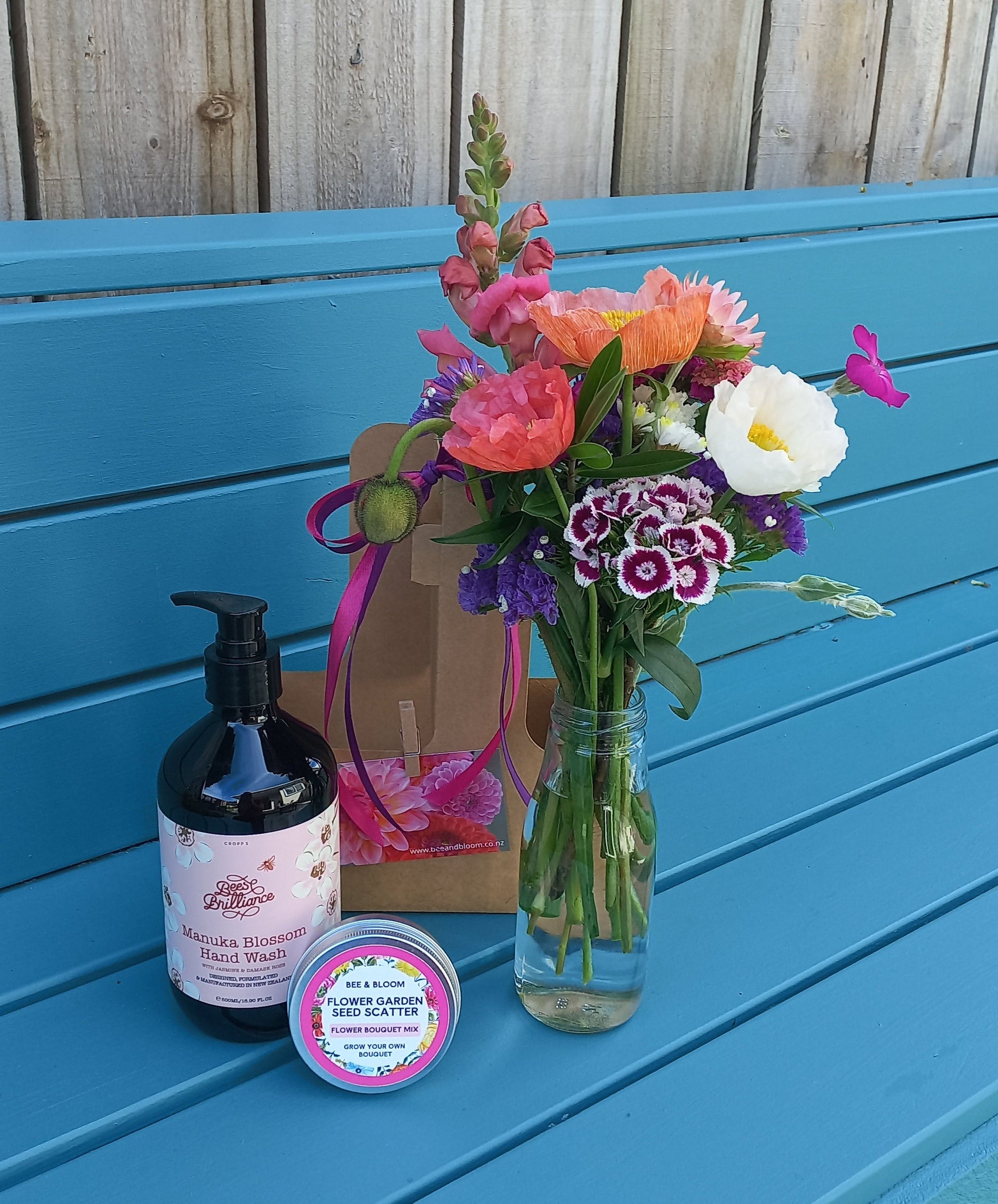 Bouquet of flowers and a bottle on a blue surface next to wooden planks.