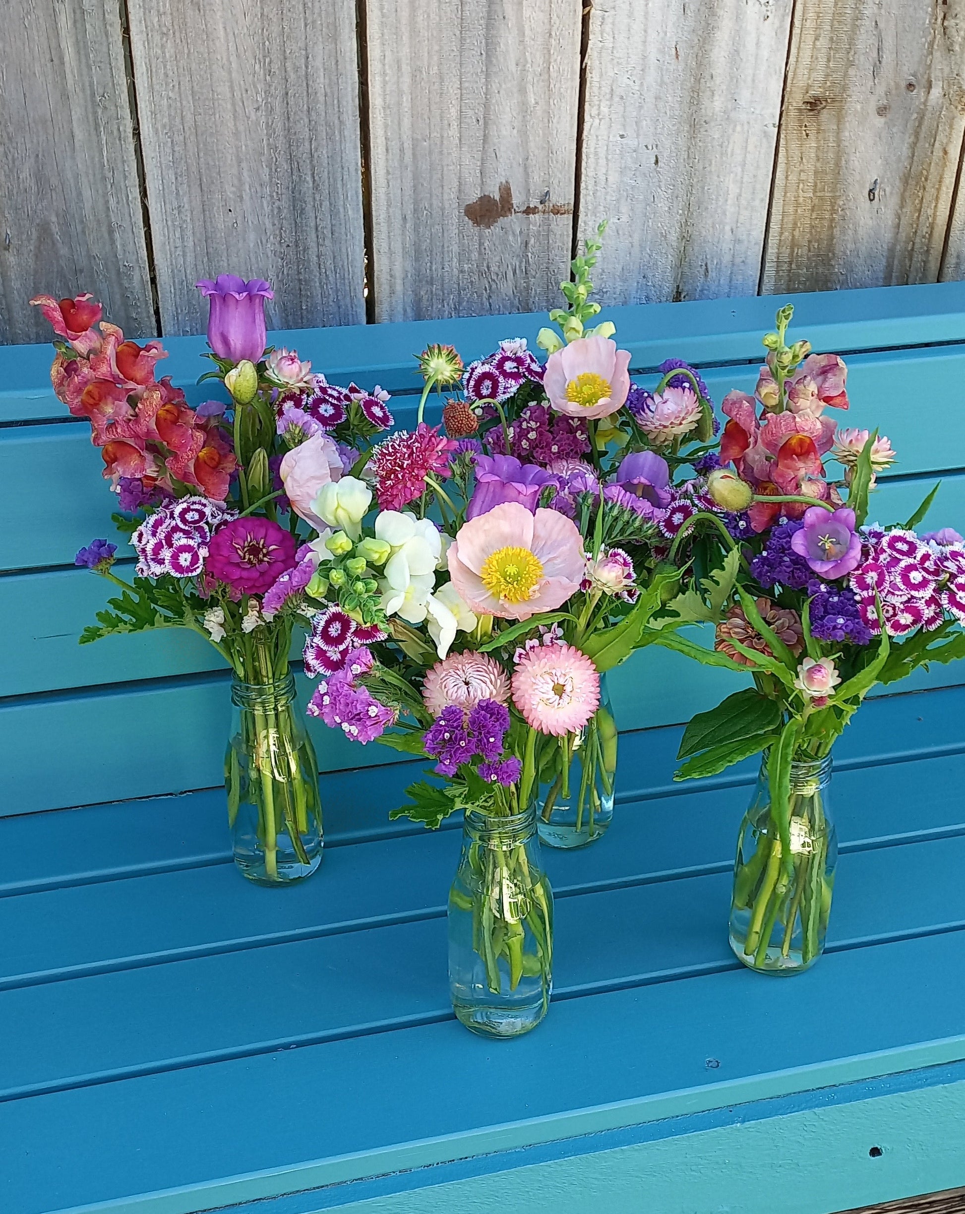 bottles of colourful flowers on a blue bench